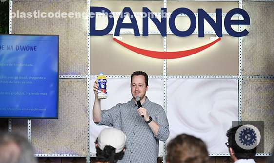 Na imagem aparece um homem de pele branca, e atrás dele está logo da Danone. A foto com um representante da empresa ressalta o objetivo da empresa em tornar seu portifólio totalmente reciclável 