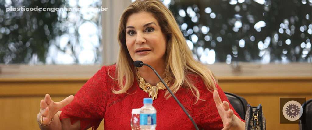 Fotografia de uma mulher loira, de pele branca, falando em um microfone. Representando o projeto "Elas na indústria". O projeto voltado para a  indústria