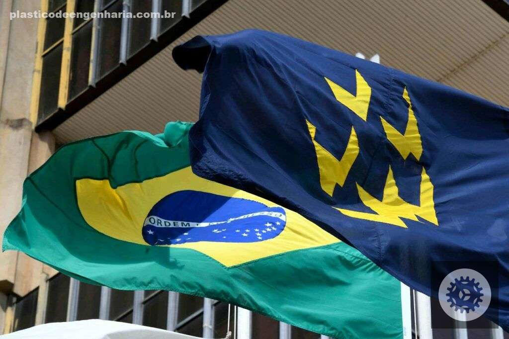 A imagem mostra duas bandeiras hasteadas em frente a um prédio. A bandeira à esquerda é a bandeira do Brasil e a bandeira à direita é a bandeira da CNI. Isso porque, o presidente, Ricardo Alban, analisa como a decisão do Banco Central afeta a indústria 